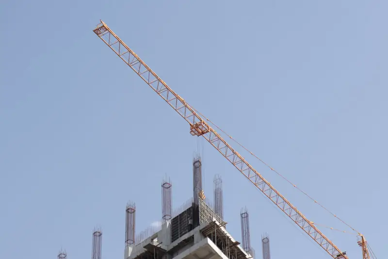 Tower crane lifting near a high-rise under a clear blue sky