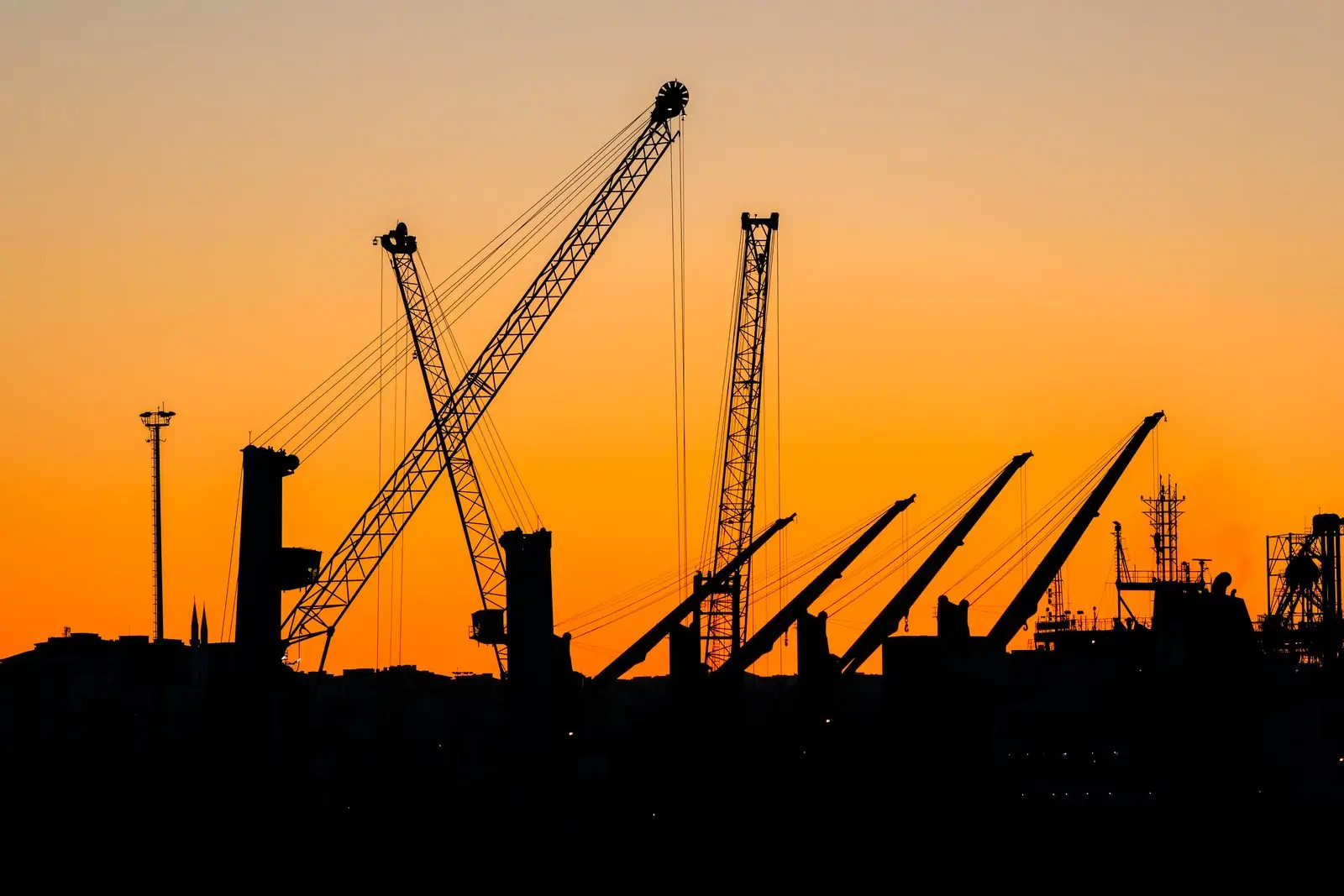 Construction cranes silhouetted against an orange sunset sky